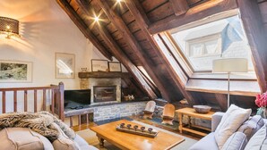 A cozy loft-style living room with a stone fireplace, wooden beams, and a large skylight. - Luderna - Casa Coto Moreu (Betren)