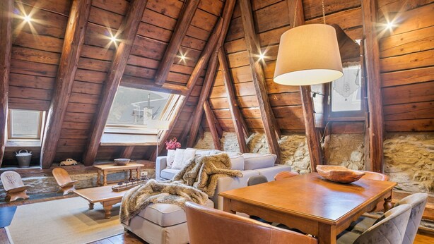 A cozy attic room with a wooden ceiling, a dining table, a sofa, and a large window. - Luderna - Casa Coto Moreu (Betren)
