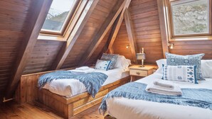 Un dormitorio acogedor en el ático con vigas de madera, dos camas con ropa de cama azul y blanca, y un gran ventanal con vistas al exterior.