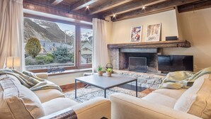 Una sala de estar acogedora con chimenea de piedra, un televisor y vistas a una montaña nevada.