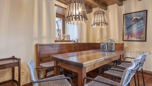 Una mesa de comedor de madera con cuatro sillas tejidas, dos lámparas colgantes y un cartel enmarcado en la pared.