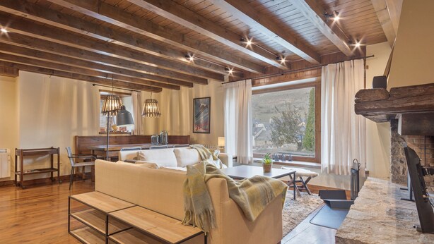 Una sala de estar acogedora con sofá, vigas de madera, chimenea de piedra y un ventanal grande.