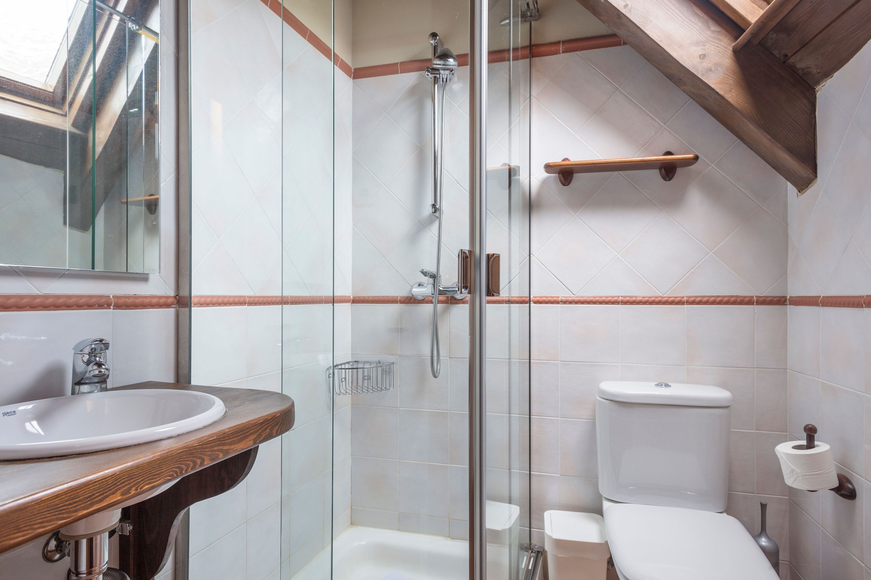 A bathroom with a glass-enclosed shower, a wooden vanity with a sink, and a toilet with a paper towel holder.