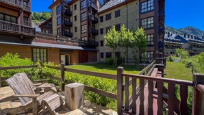 A multi-story building with balconies, stone walls, and a wooden deck with chairs. - Luderna - Apartamento Val de Ruda B25 Sarraèra (Baqueira)