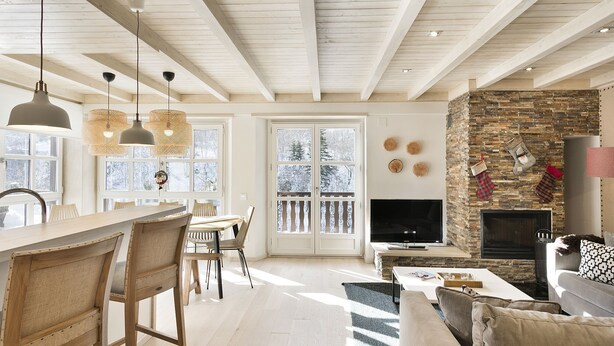A spacious living area with a stone fireplace, wooden ceiling beams, and a large window overlooking a snowy landscape. - Luderna - Apartamento Val de Ruda B25 Sarraèra (Baqueira)