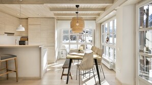 A modern kitchen with wooden beams, a dining area with a table and chairs, and large windows offering a view of the outdoors. - Luderna - Apartamento Val de Ruda B25 Sarraèra (Baqueira)