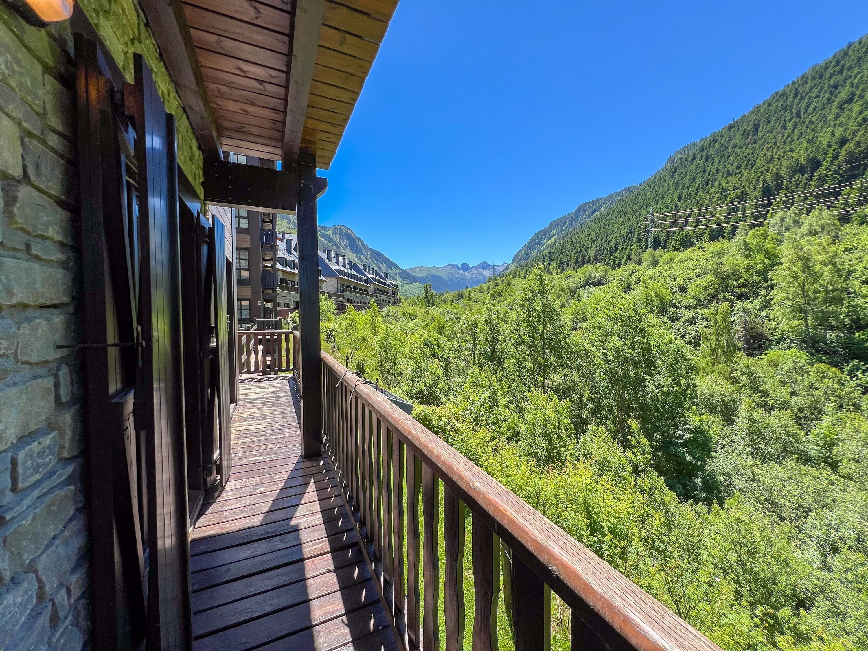 A wooden balcony with a view of a lush green valley and mountains.
