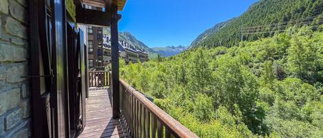 A wooden balcony with a view of a lush green valley and mountains.