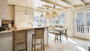 A spacious kitchen with wooden beams, a large island with bar stools, pendant lights, and a view of snowy trees through large windows. - Luderna - Apartamento Val de Ruda B25 Sarraèra (Baqueira)