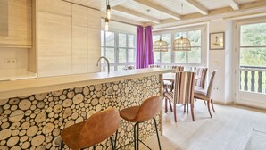 A kitchen with a wooden ceiling, a stone wall backsplash, and a bar area with two stools. - Luderna - Val de Ruda B52 dera Montjòia (Baqueira)