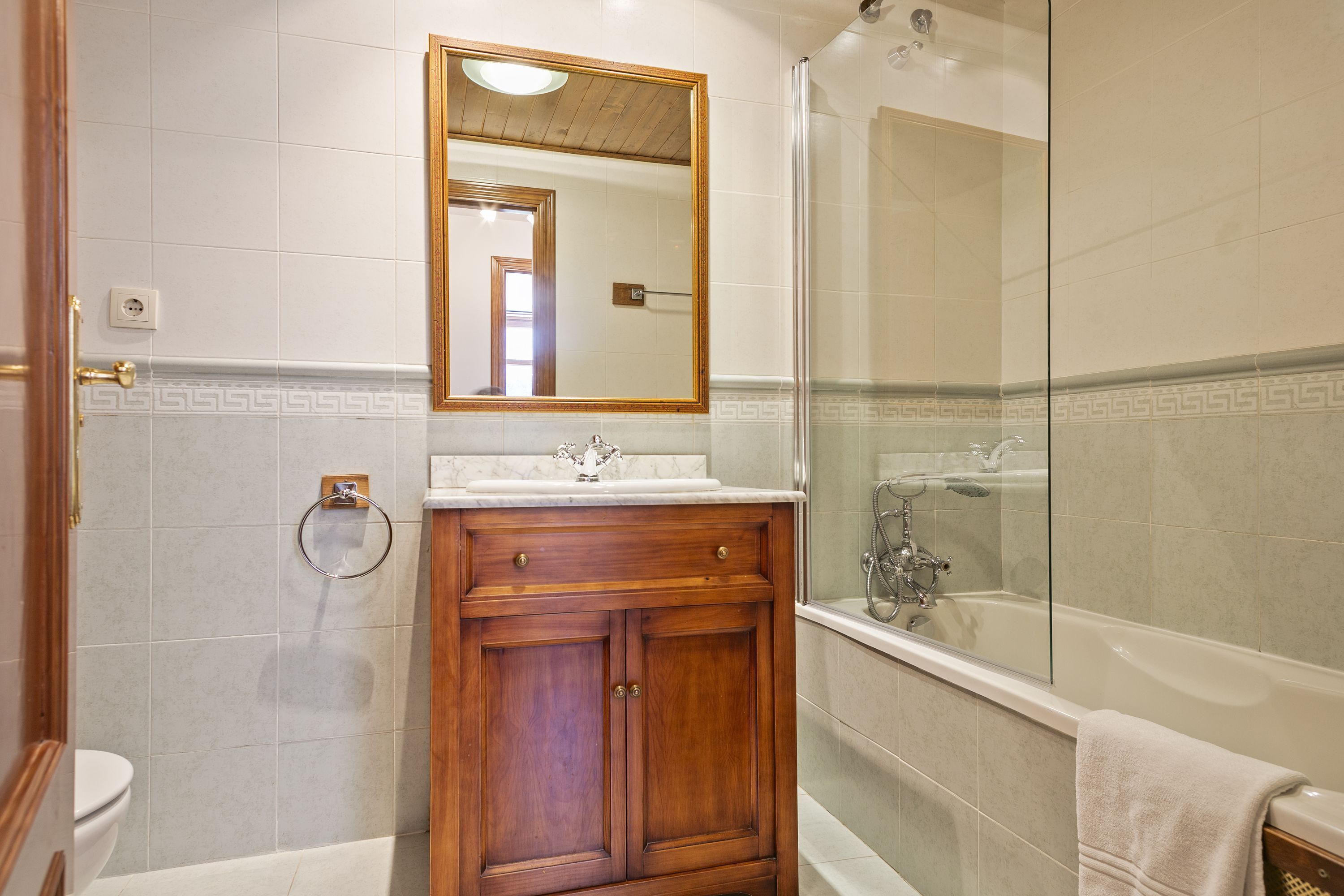A bathroom with a wooden vanity, a mirror, a toilet, and a glass-enclosed shower area.