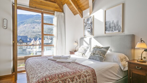 Ein Schlafzimmer mit einem großen Bett, einem Nachttisch, einer Lampe und Blick auf eine verschneite Landschaft durch ein Fenster.