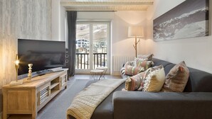 Een moderne woonkamer met een flatscreen-tv, een houten tv-meubel, een grijze bank en een groot schilderij aan de muur.