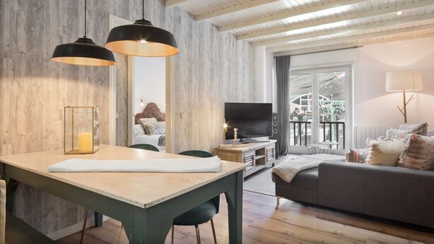 Een moderne woonkamer met een houten wand, een eethoek met een tafel, een bank en een televisie.
