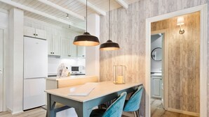 Een moderne keuken met witte kastjes, een wand met houten accenten, en een eethoek met tafel en stoelen.