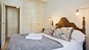 Een keurig opgemaakt bed met een grijze deken en witte kussens, een houten hoofdbord en een wandlamp.