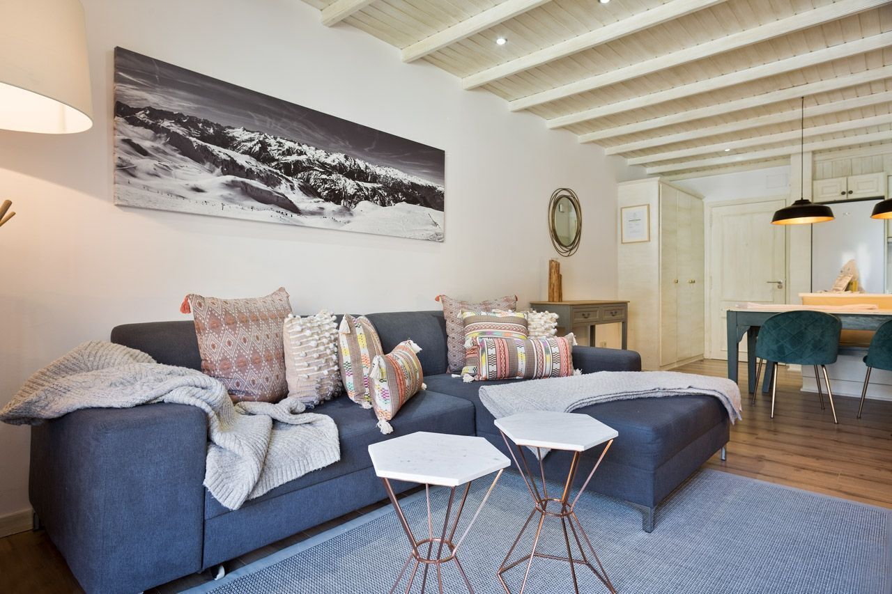 A modern living room with a grey sofa, patterned cushions, a white coffee table, and a large black-and-white mountain landscape painting on the wall.