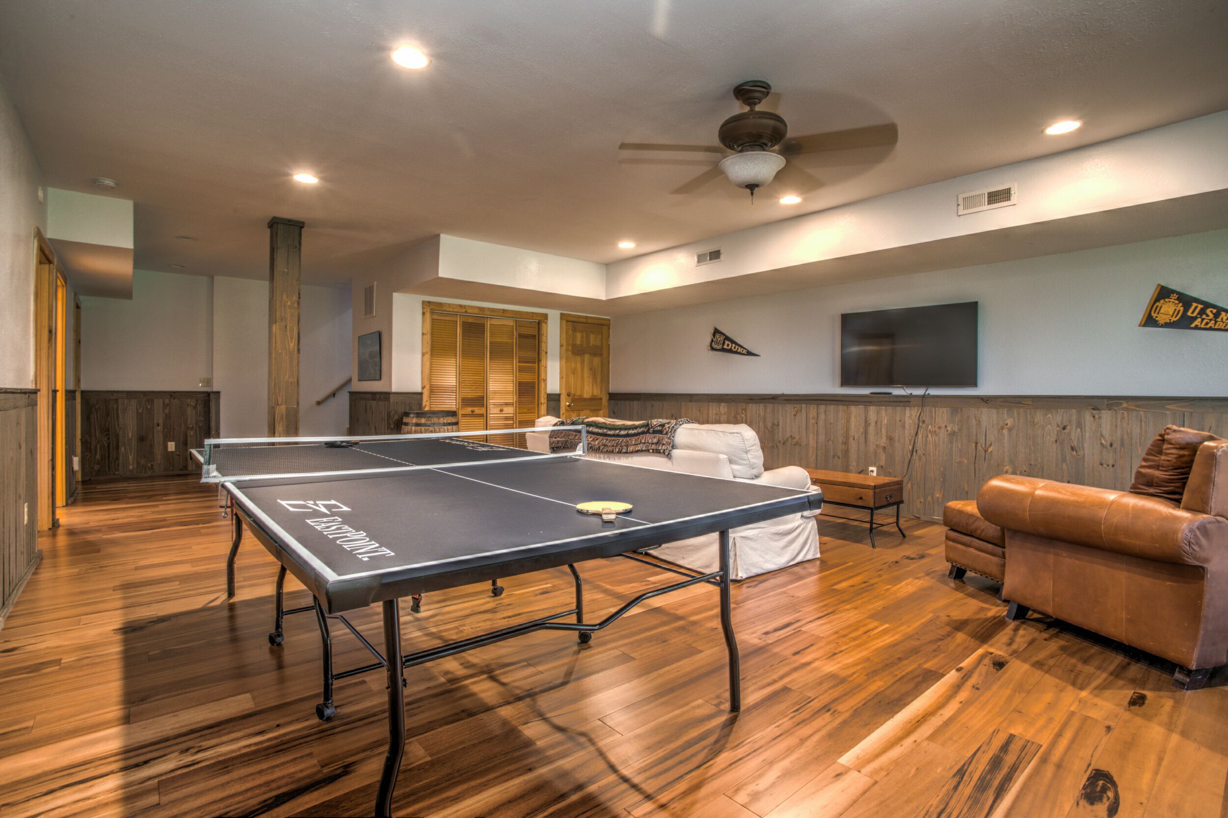 A spacious room with a ping pong table, a sofa, a TV, and wooden flooring.