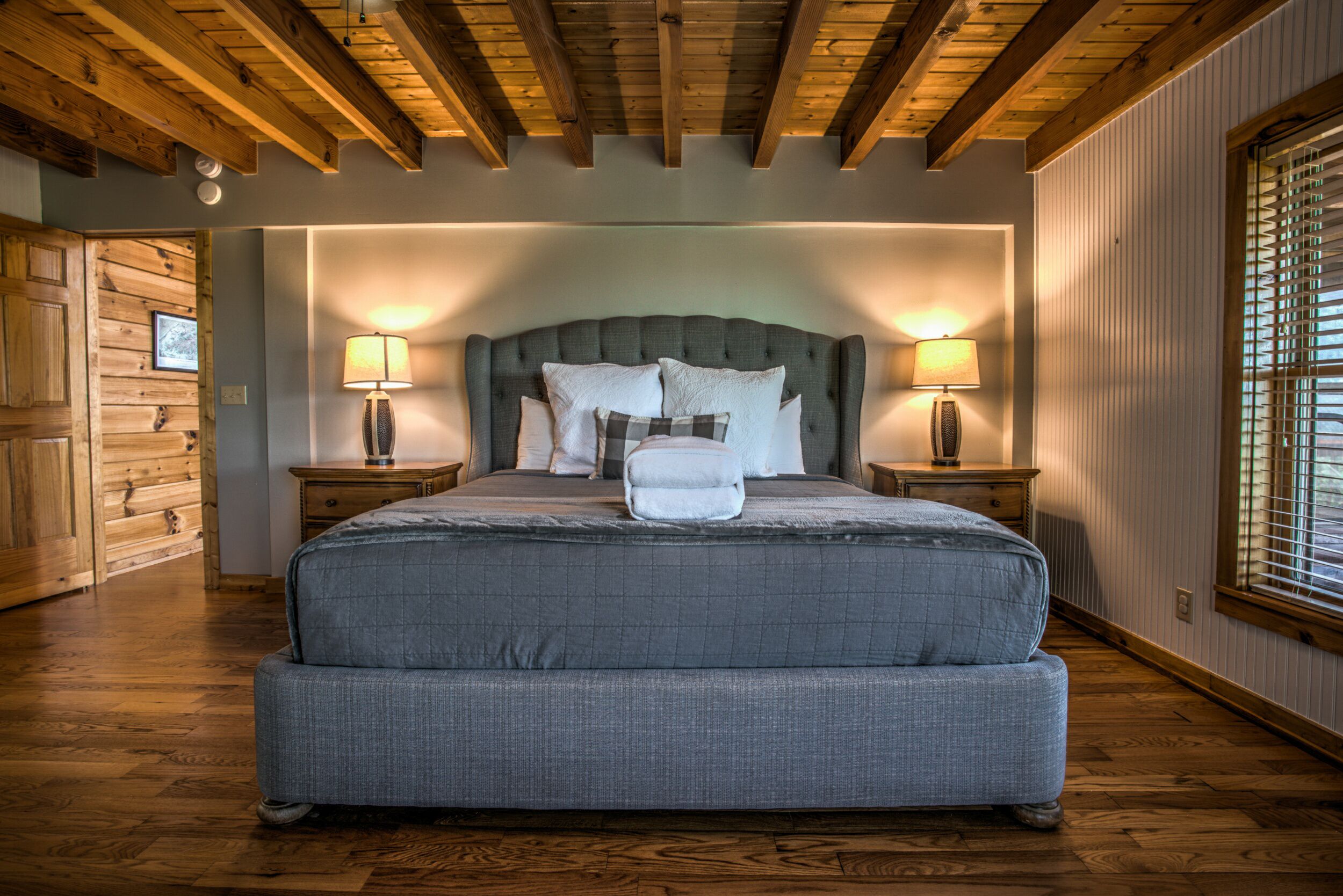 Ein großes Bett mit grauem Polsterkopfstück, zwei Nachttische mit Lampen und Holzboden.