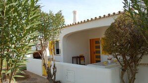En vit byggnad med ett tak täckt av tegelpannor, en trädörr och ett litet bord med en stol.