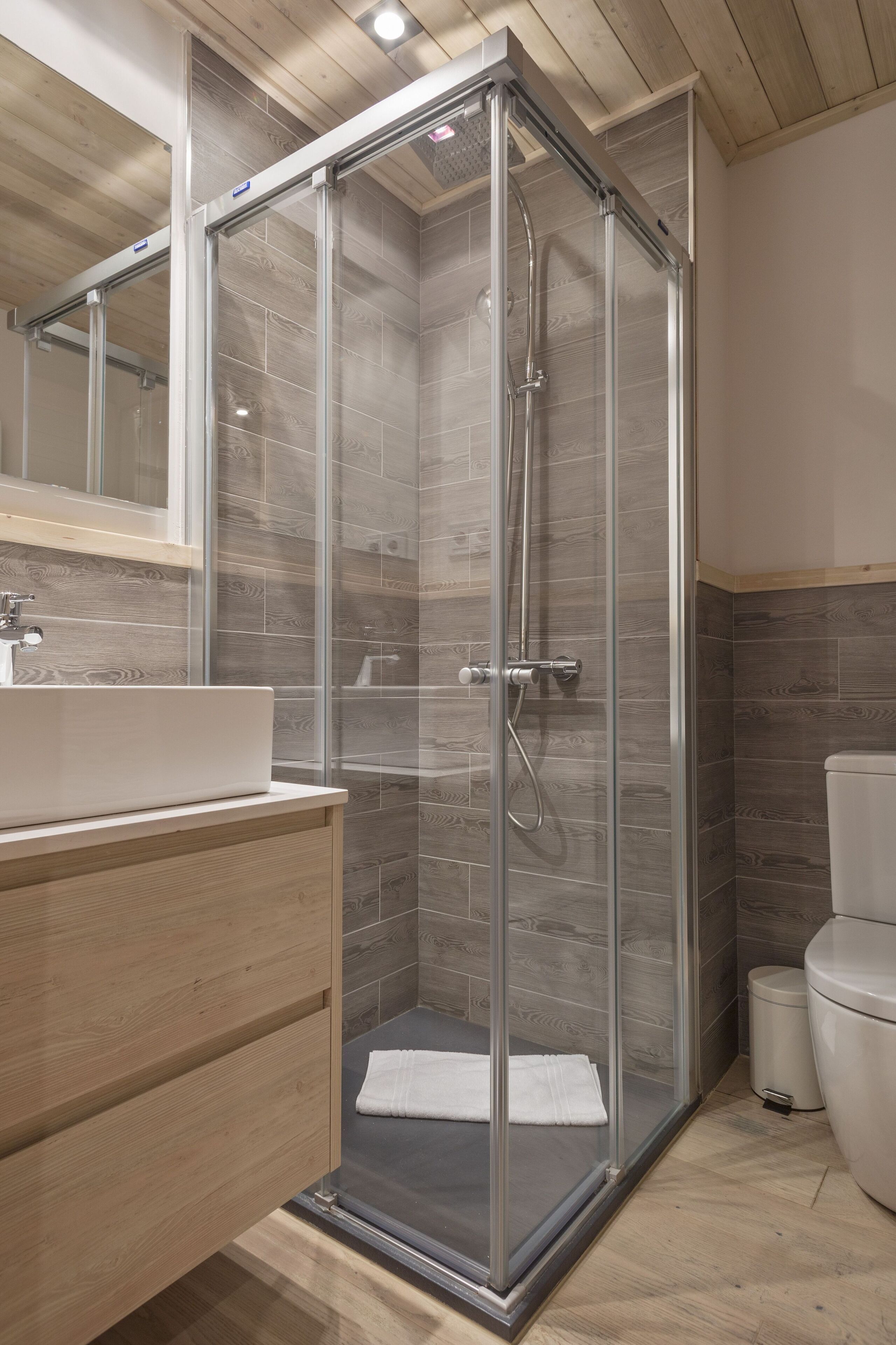 Une salle de bain moderne avec une douche à parois de verre, un meuble-lavabo en bois et des toilettes.