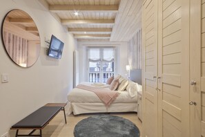 Una camera da letto con un letto, una panca, uno specchio tondo, una televisione e un armadio.