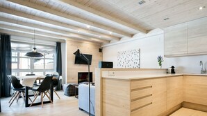 Une cuisine moderne avec des meubles en bois, un coin repas comprenant une table et des chaises, et une grande fenêtre laissant entrer la lumière naturelle.