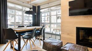 Un espace repas moderne avec une table en bois, des chaises noires et un pouf à carreaux.