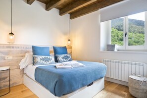 A bedroom with a bed, bedside tables, a window with a view of greenery, and a radiator. - Luderna - Dúplex con jardín des Treuetes (Gessa)