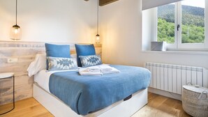 Ein Schlafzimmer mit Bett, Nachttischen, einem Fenster mit Blick ins Grüne und einer Heizung.