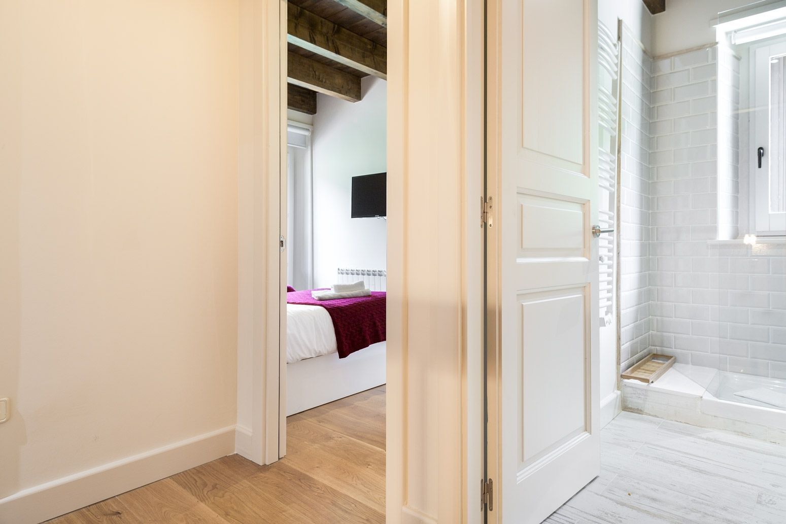 A hallway leading to a bedroom with a bed, a bathroom with a bathtub, and a shower area.