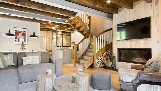 Ein gemütliches Wohnzimmer mit einer Couch, Hocker, einem Kamin, einem Fernseher und einer Holztreppe.