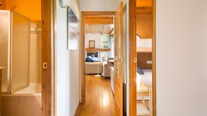 Un pasillo estrecho que conduce a un dormitorio con literas, suelo de madera y un pequeño rincón de descanso con una mesa y sillas.