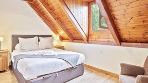 A bedroom with a wooden ceiling, a bed with white linens, a nightstand, a chair, and a window. - Luderna - Casa con jardín Vista Aneto (La Val d'Aran)