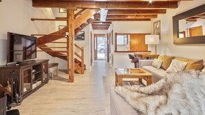 A spacious living area with a wooden staircase, a television, a sofa with a fur throw, and a dining table. - Luderna - Casa con jardín Vista Aneto (La Val d'Aran)