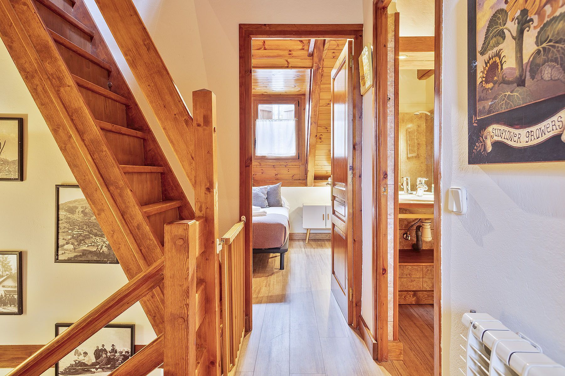 Una escalera de madera que lleva a un dormitorio con una cama, una mesita de noche y una ventana.