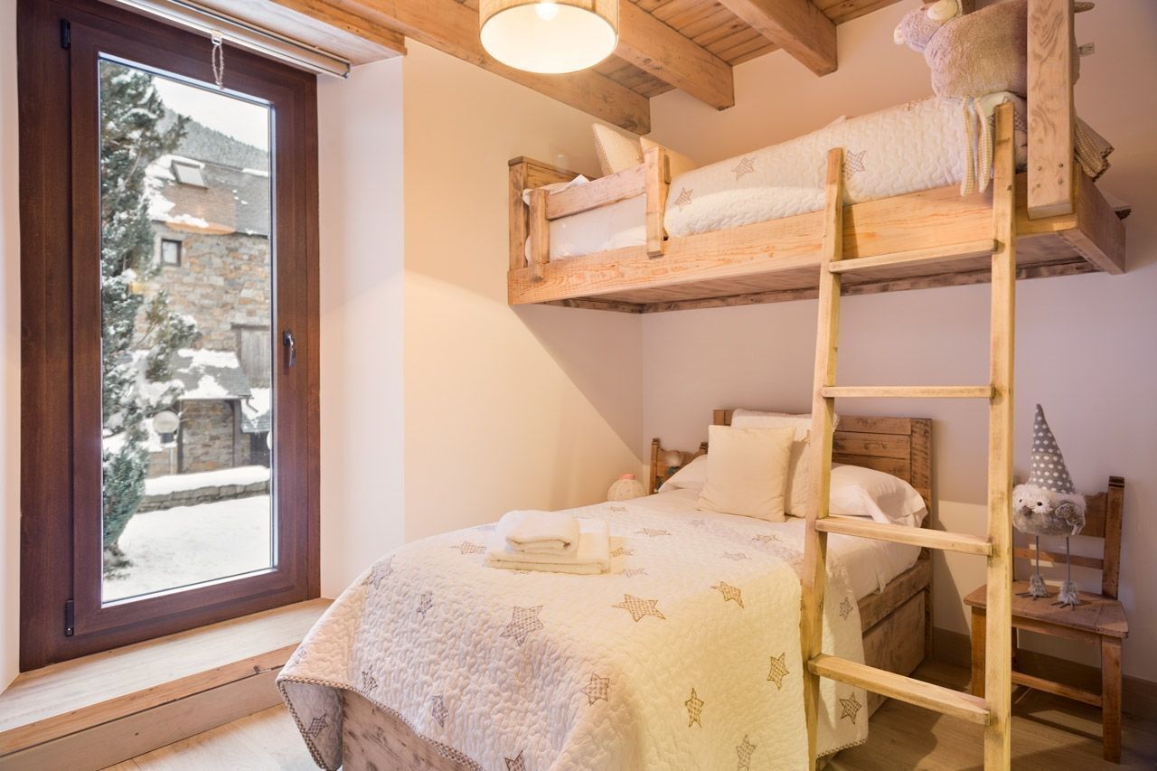 Ein gemütliches Zimmer mit einem Etagenbett, einer Leiter, einem Fenster mit Blick auf eine verschneite Landschaft und einem kleinen Tisch mit einem dekorativen Gegenstand.