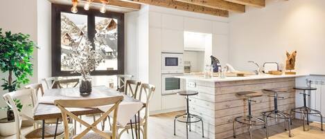 A modern kitchen with white cabinetry, a wooden dining table with chairs, and a bar area with stools.
