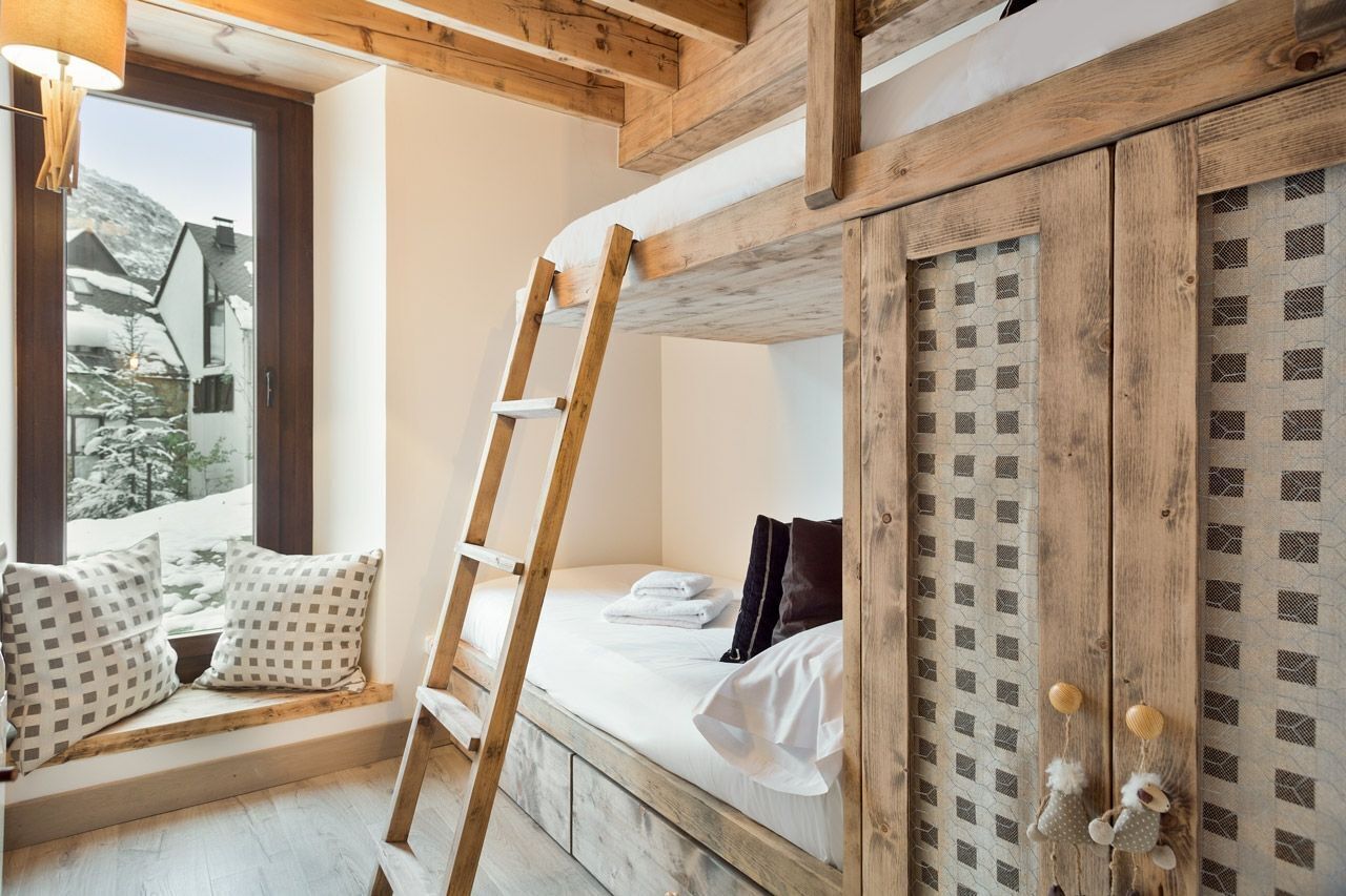 A cozy room with a bunk bed, a ladder, a window with a view of a snowy landscape, and a wooden wardrobe with a patterned door.
