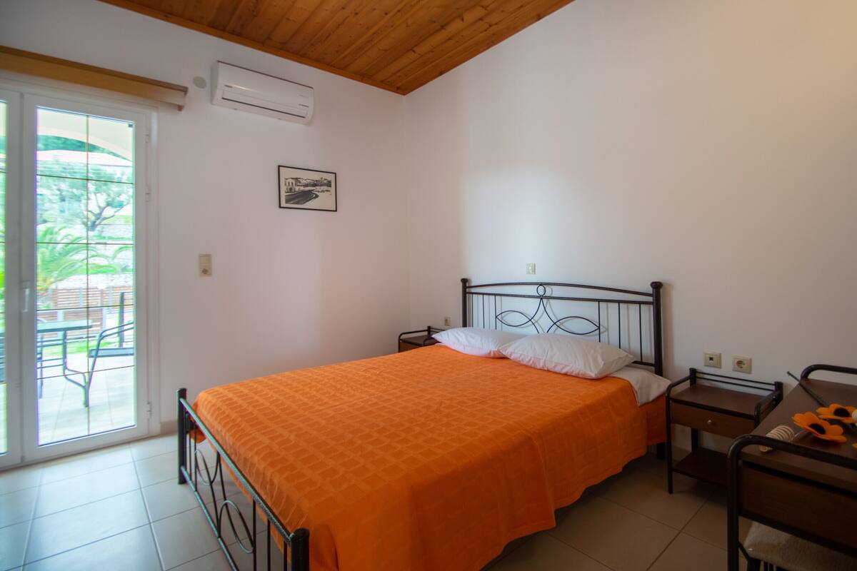 A bedroom with a bed, a nightstand, a desk, and a window.