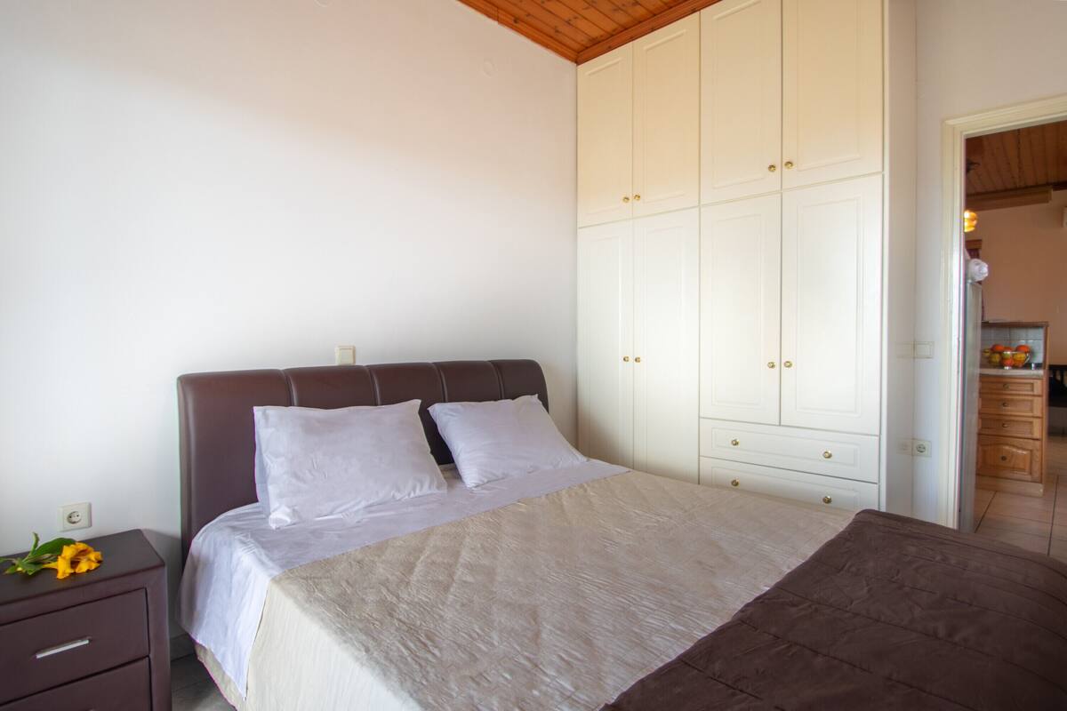 A bedroom with a bed, a nightstand, a wardrobe, and a wooden ceiling.