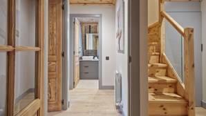 A hallway with wooden flooring, a staircase with wooden railings, and a view into a bathroom with a sink and mirror. - Luderna - Val de Ruda C23 Barbacans (Baqueira)