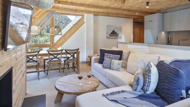 A modern interior with a wooden ceiling, a dining area with a table and chairs, a sofa with patterned cushions, and a kitchen area. - Luderna - Val de Ruda C23 Barbacans (Baqueira)