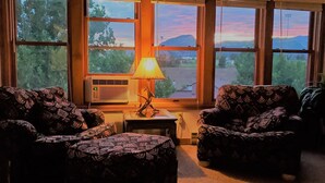 A room with two patterned armchairs, a small table with a lamp, and an air conditioning unit. - Durango Treehouse | Mountain Views | Hot Tub (Durango)