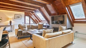 Un loft amplio con techo alto, vigas de madera, un sofá, una mesa de comedor y un televisor.