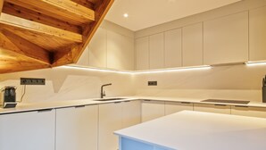 Una cocina moderna con armarios blancos, techo de madera e iluminación debajo de los gabinetes.
