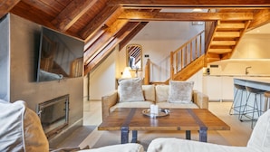 Un acogedor espacio tipo loft con techo de madera, chimenea, sofá, mesa de centro y área de cocina con taburetes de bar.