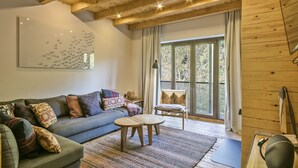 Un salon chaleureux avec un plafond en bois, une grande fenêtre, un canapé, une table basse et un fauteuil.