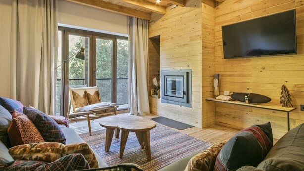 Un salon chaleureux avec une cheminée, un grand téléviseur et un coin salon confortable comprenant un canapé et des fauteuils.