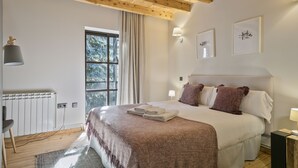 Une chambre avec un plafond en bois, un grand lit avec des oreillers, une fenêtre avec des rideaux et des lampes fixées au mur.